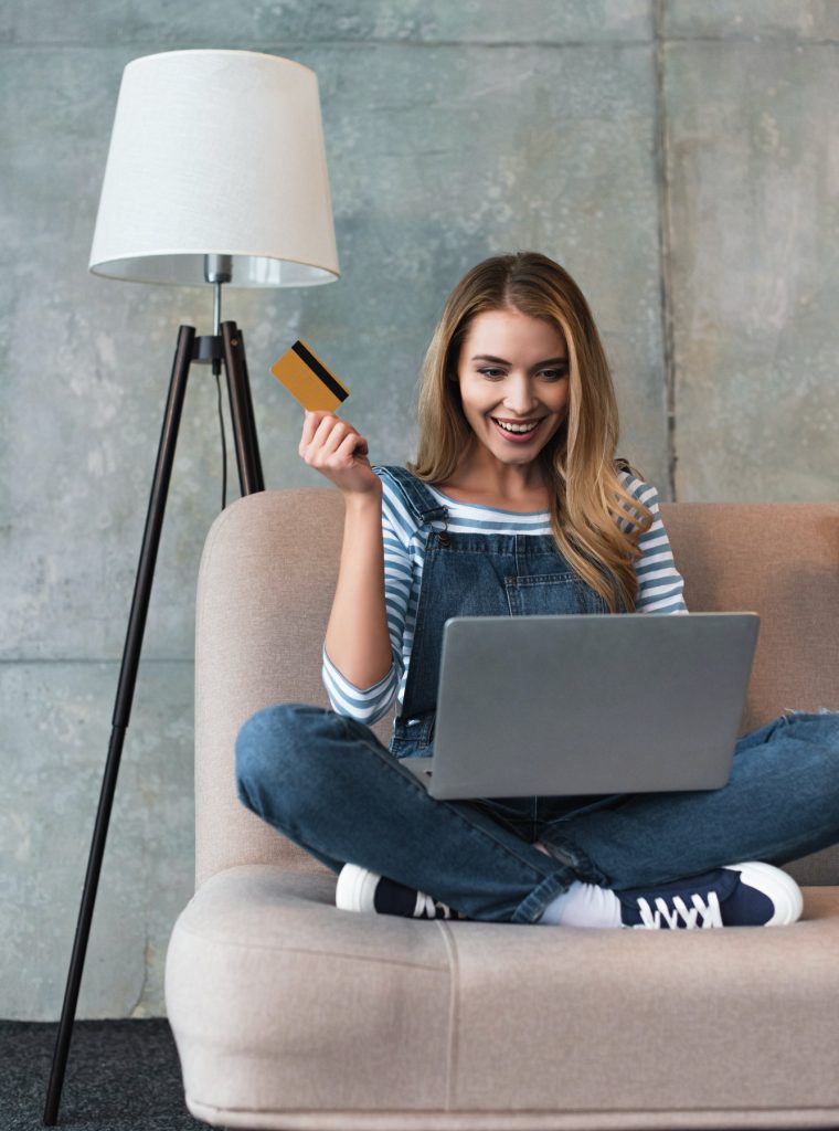 happy-beautiful-woman-holding-credit-card-in-hand-and-sitting-on-sofa-with-laptop.jpg